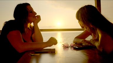 Zwei Frauen sitzen an einem Tisch bei Sonnenuntergang.