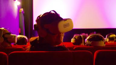 In einem Kinosaal sieht man Personen, die Kopfhörer und VR-Brillen tragen.