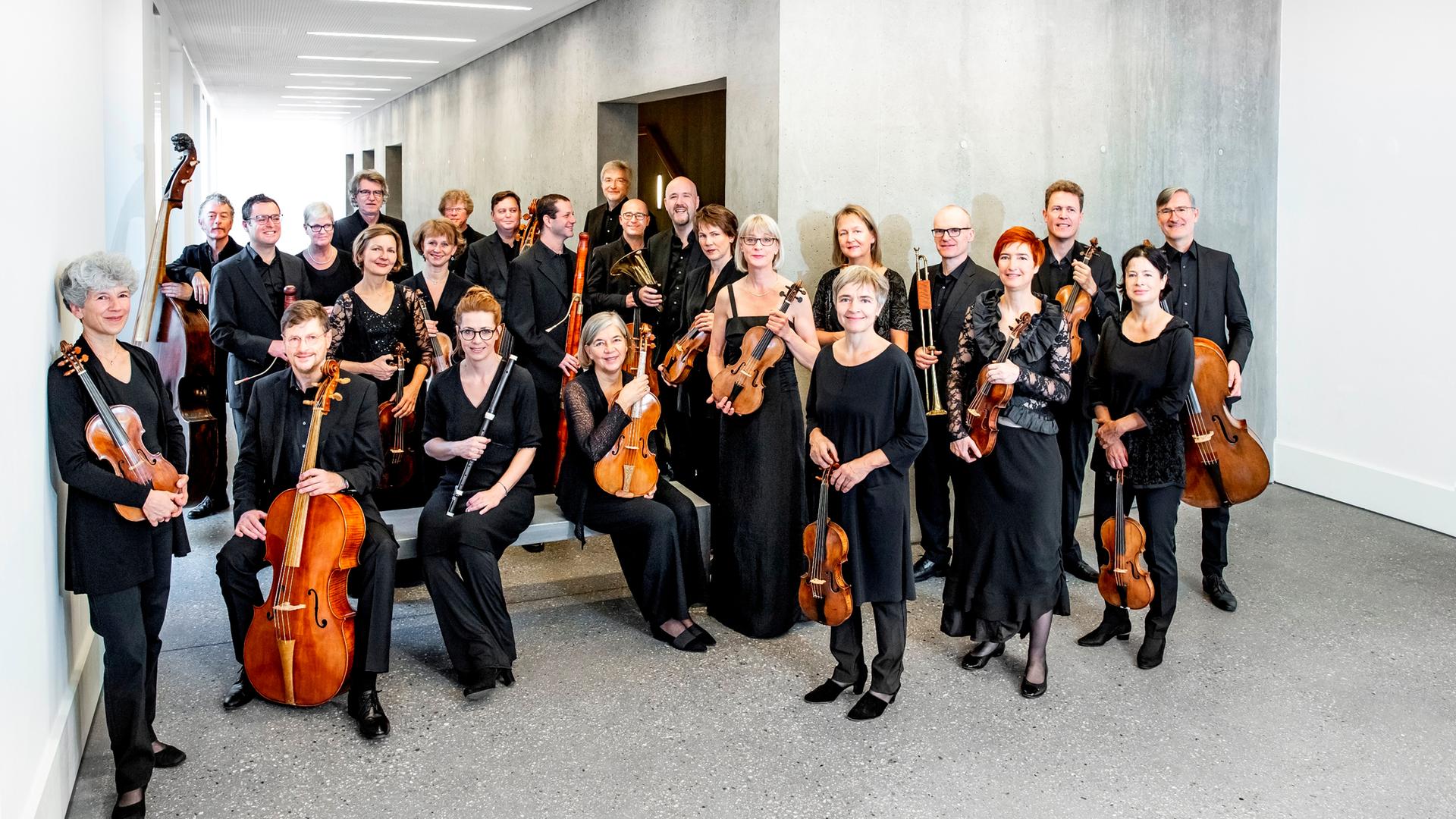 Die Mitglieder eines großen Streich-Orchesters haben sich für ein Gruppenfoto in einem modernen Vorraum versammelt.