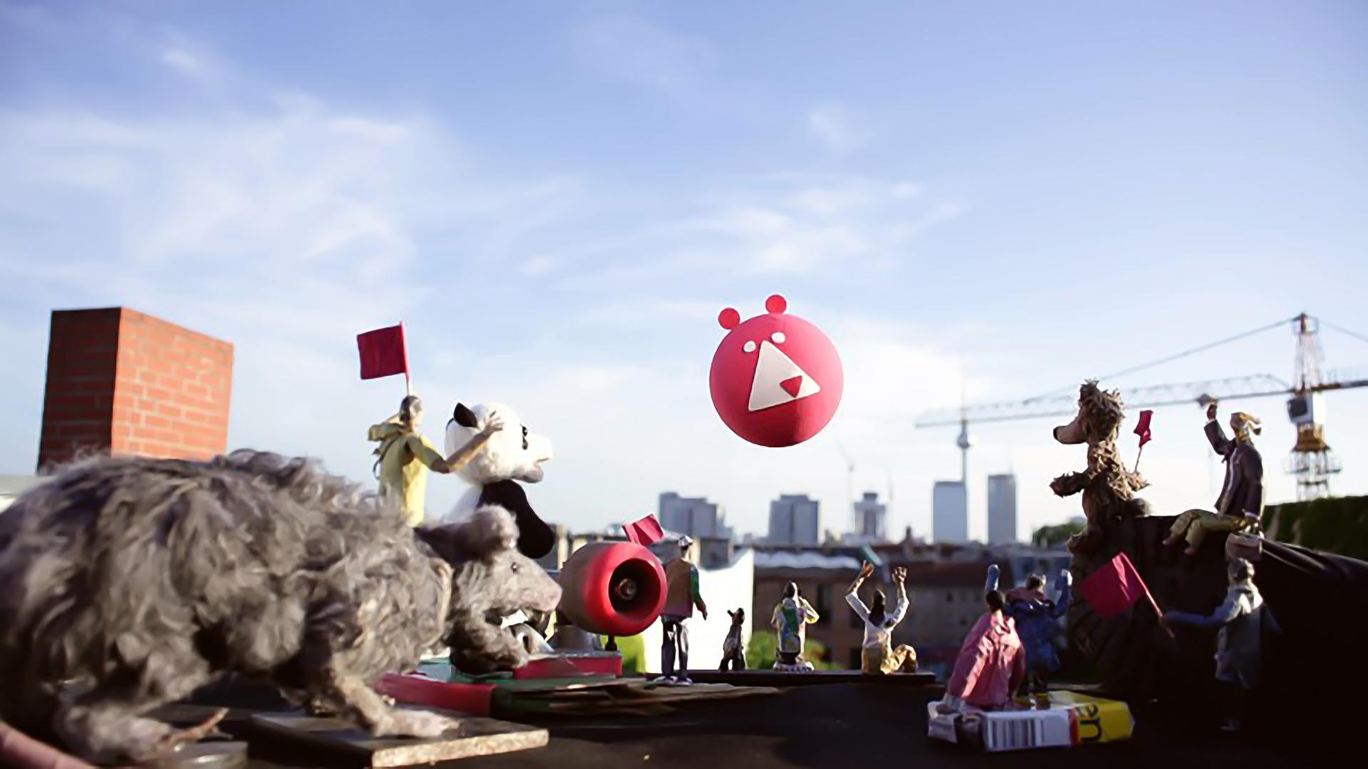 Viele kleine Figuren und Kinderspielzeuge stehen auf einem Tisch und blicken in Richtung einer Skyline, wo auch ein Ballon langfliegt.