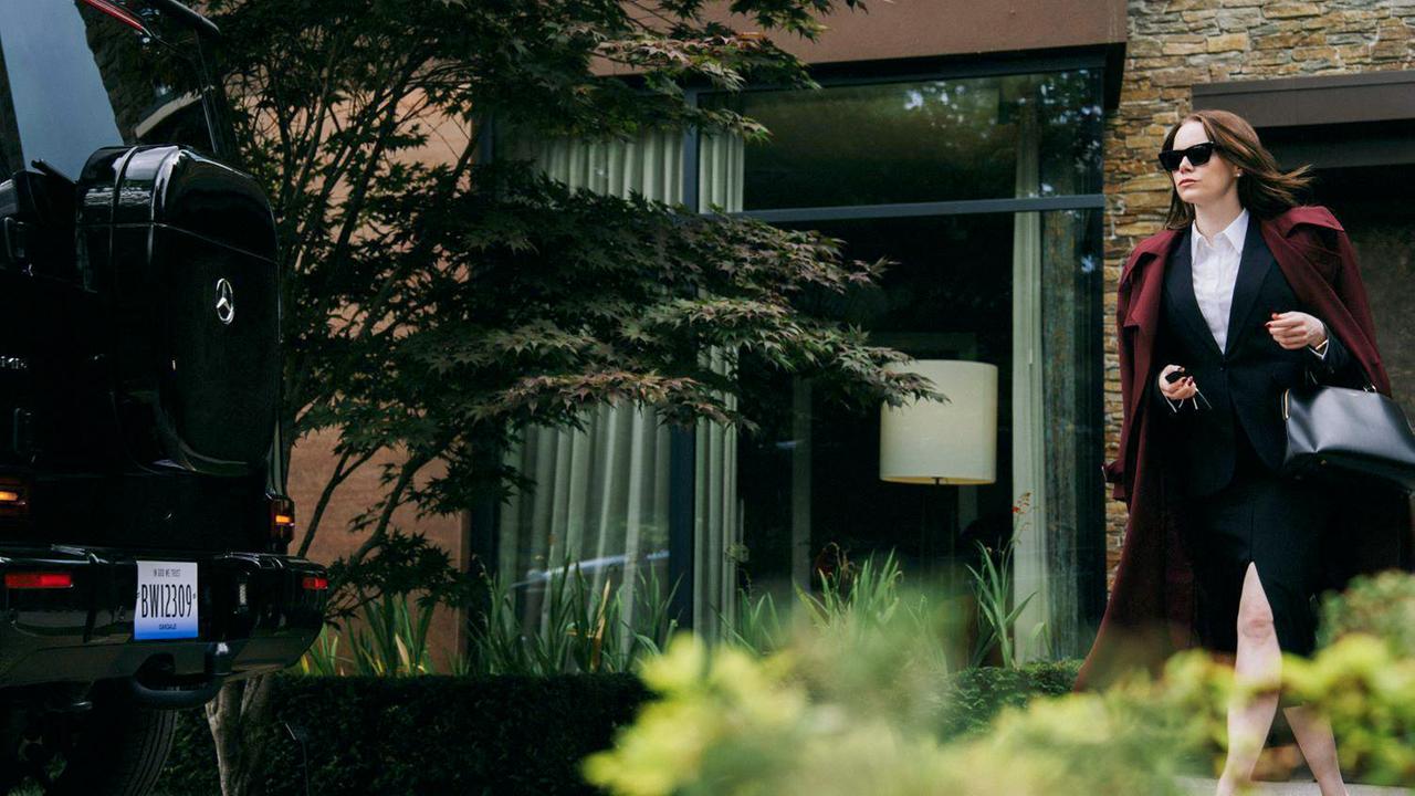 Eine Frau, die ein Businesskostüm und Sonnenbrille trägt, geht zu einem Auto.