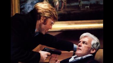 Ein Mann bedroht einen zweiten am Boden liegenden mit einer Pistole.