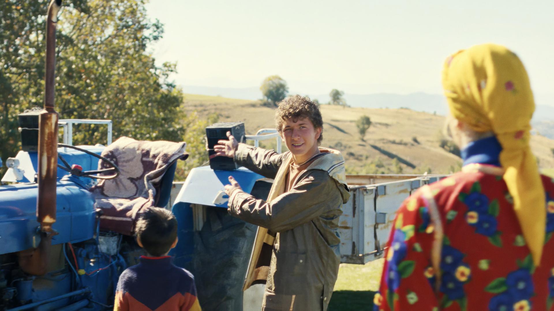 Ein junger Mann steht vor einem Traktor. Neben ihm steht eine Person in Tracht.