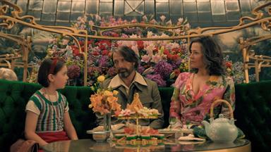 Ein Mädchen, ein Mann und eine Frau sitzen an einer im Art-Nouveau-Stil geschmückten Kaffee-Tafel.