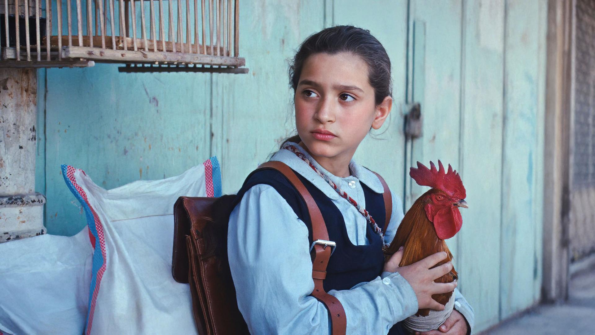 Ein Mädchen hält einen Hahn auf dem Arm.