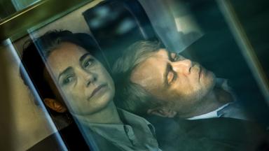 Eine Frau schaut aus einem Fenster, an ihrer Schulter lehnt ein Mann mit geschlossenen Augen.