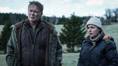 Ein Mann und eine Frau stehen in winterlicher Kleidung vor einem Waldstück.