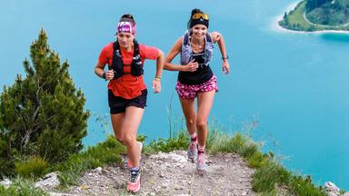 Zwei Frauen in Sportbekleidung laufen auf einem Bergweg.