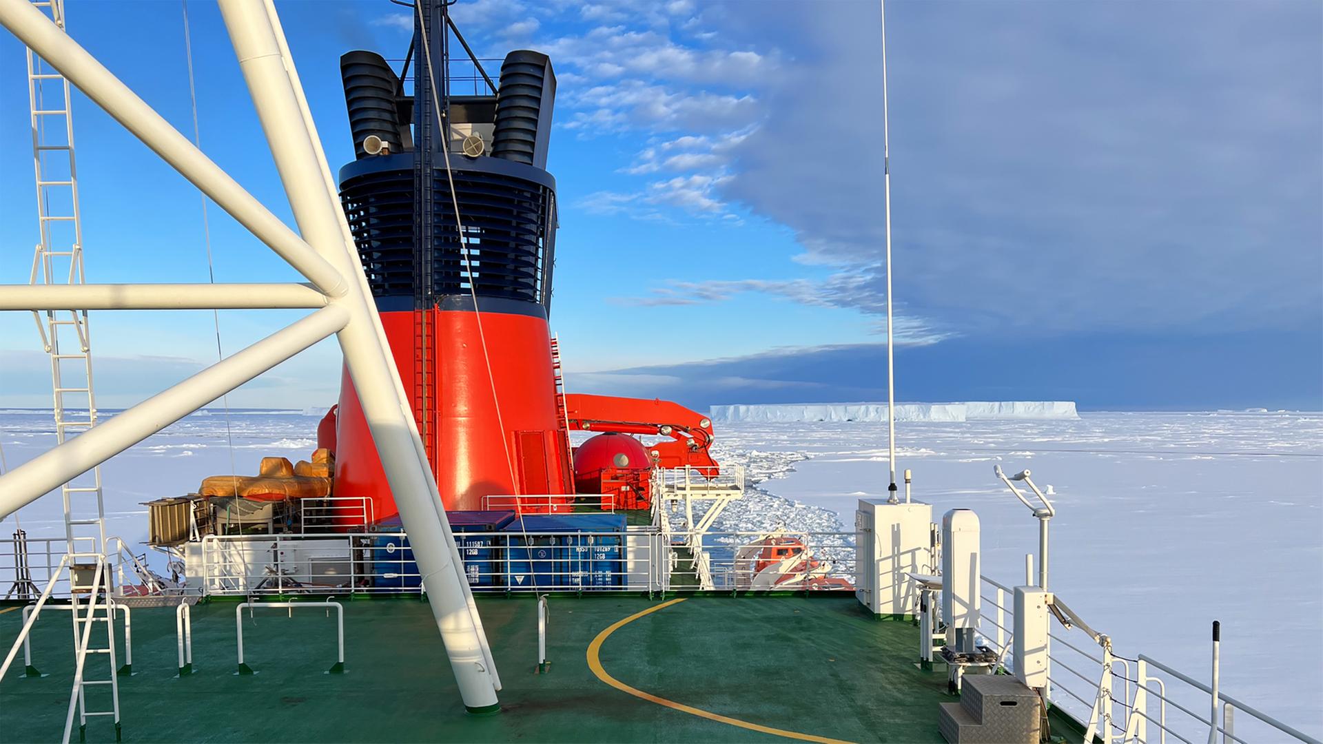 Blick von einem Eisbrecher auf das Polarmeer, auf dem eine Eisschicht liegt.