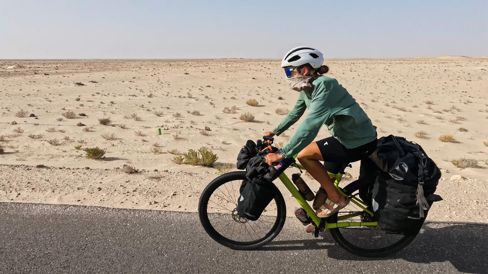 Eine Frau fährt mit dem Fahrrad durch die Wüste.