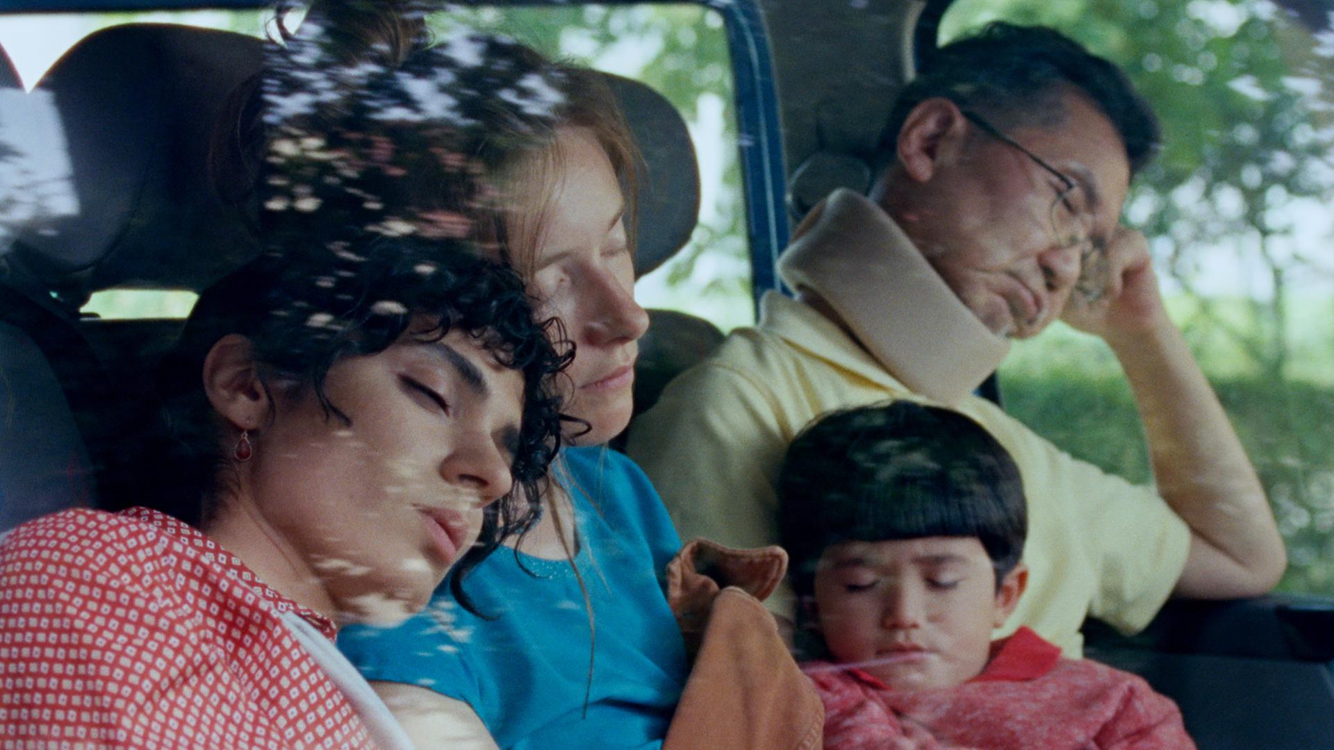 Auf der Rückbank eines Autos sitzen ein Mann, zwei Frauen und ein Kind und schlafen.