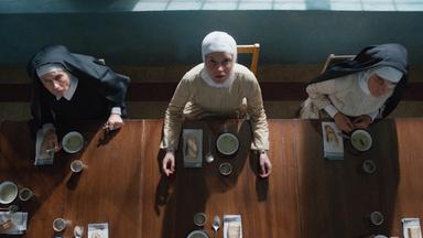 Blick von schräg oben auf drei Nonnen, die an einem Tisch sitzen und Teller vor sich haben.