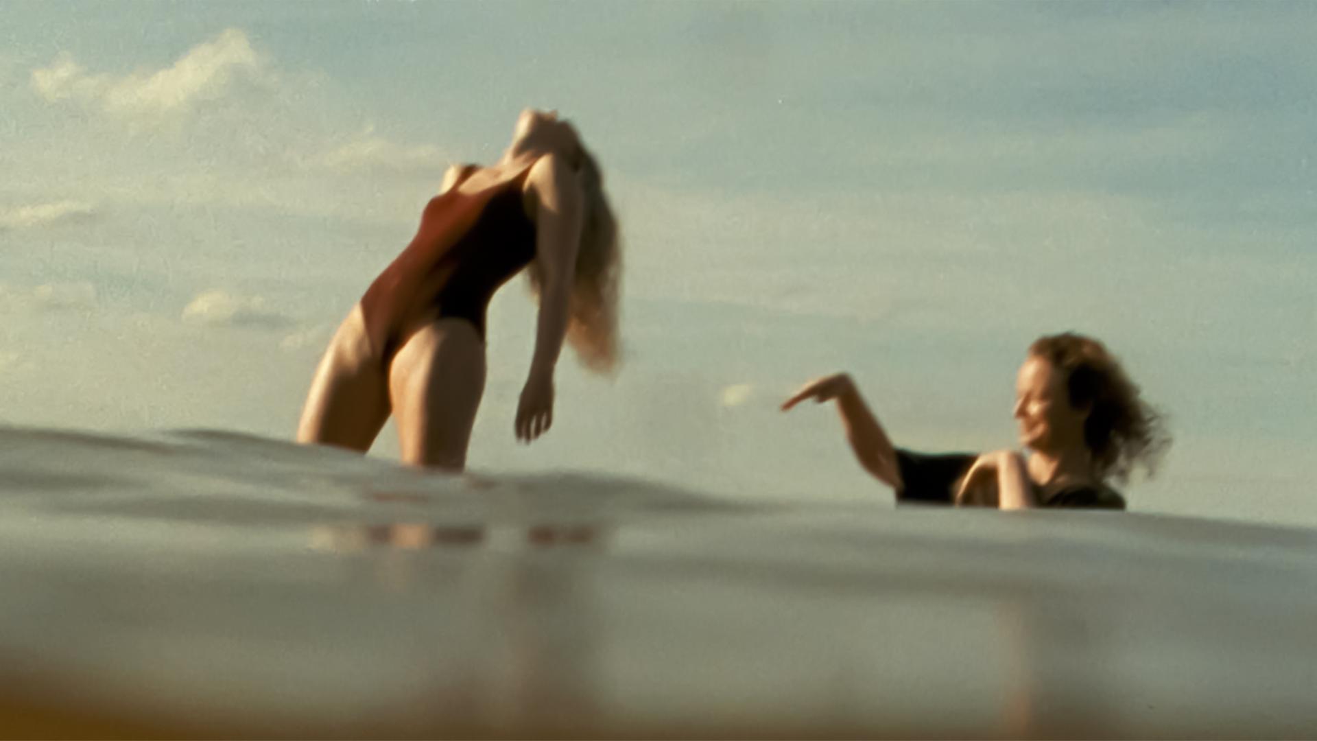 Zwei Frauen im Meer, eine steht, eine badet.