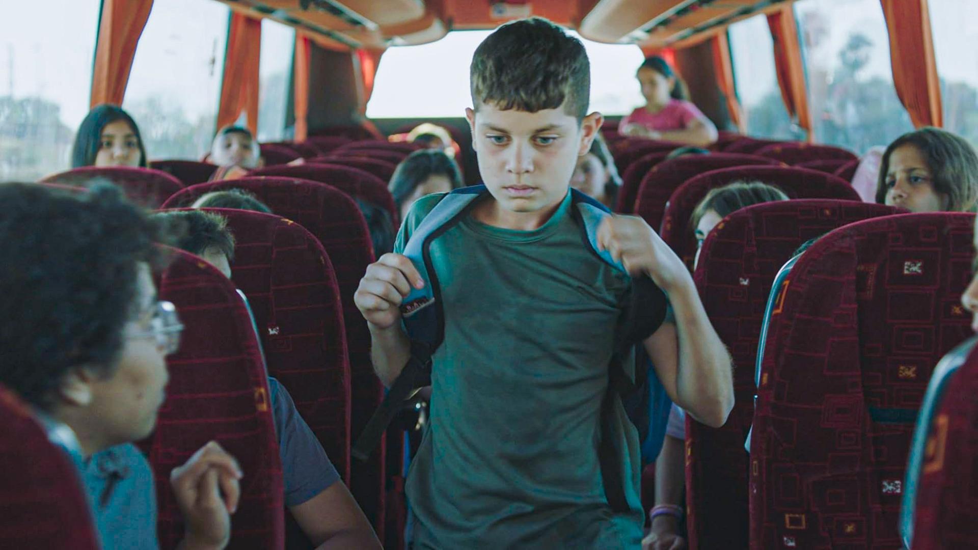 Ein junge mit Schulranzen auf dem Rücken geht durch den Gang zwischen den Sitzreihen in einem Bus.