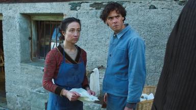 Eine Frau und ein Mann stehen vor einem alten Steinhaus.