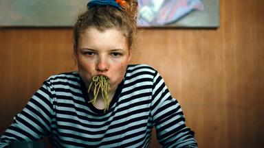 Eine junge Frau hat sich den Mund mit Spaghetti vollgestopft und blickt grimmig in die Kamera.