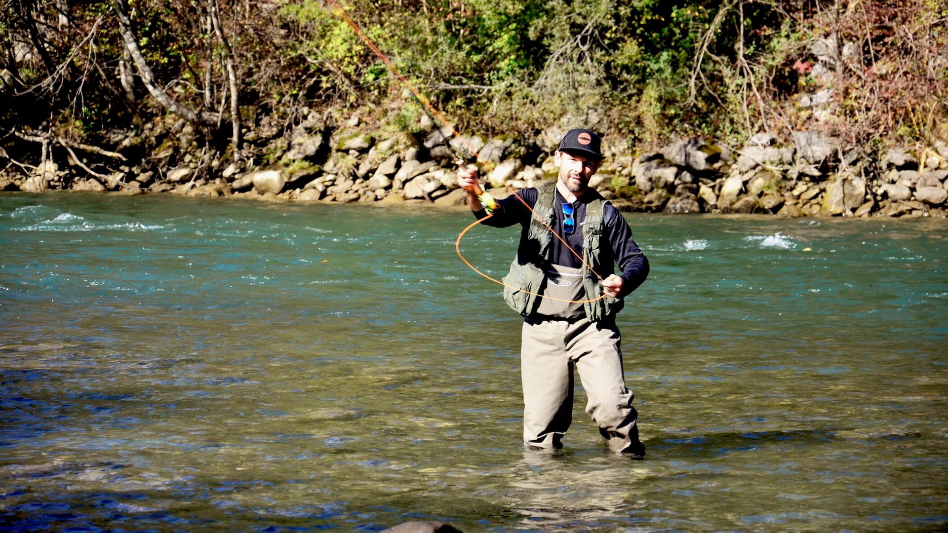 Ein Angler steht bis zu den Knien im Wasser und fischt in einem Bergfluss