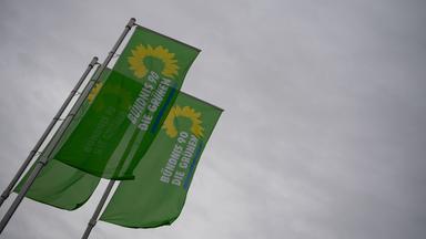 Drei große grüne Flaggen, in deren Mitte in weißen Lettern "Bündnis 90 Die Grünen" geschrieben steht, wehen vor einem bewölkten Himmel.
