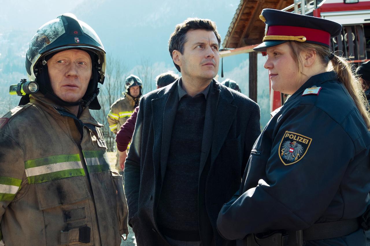 Ein Feuerwehrmann in Montur, ein Mann in dunkler Kleidung und eine Polizistin in Uniform stehen beieinander