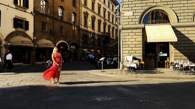 Eine Frau in rotem Kleid steht in einer italienischen Straße.