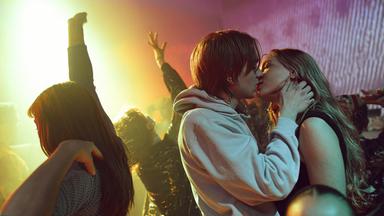 Ein junges Paar küsst sich in einer tanzenden Menschenmenge.