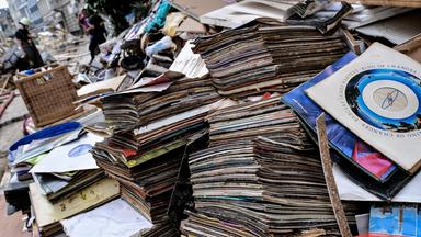 Zwischen gestapelten Gegenständen bewegen sich Menschen, die nach der Flut in Stolberg beim Aufräumen helfen.