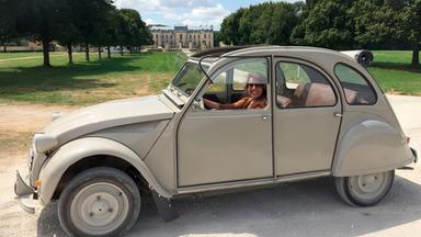 Eine Frau in einem alten Auto vor einem Schloss.