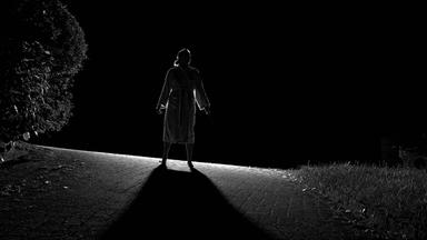 Eine Frau steht bei Nacht auf einer Anhöhe mit dem Rücken zum Betrachter und wird von vorne angeleuchtet, so dass sie als Schattenriss zu sehen ist.