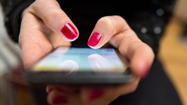 Zwei Hände mit rotlackierten Fingernägeln halten ein Smartphone.