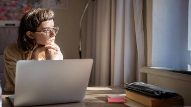 Frau sitzt nachdenklich am Schreibtisch und schaut aus dem Fenster
