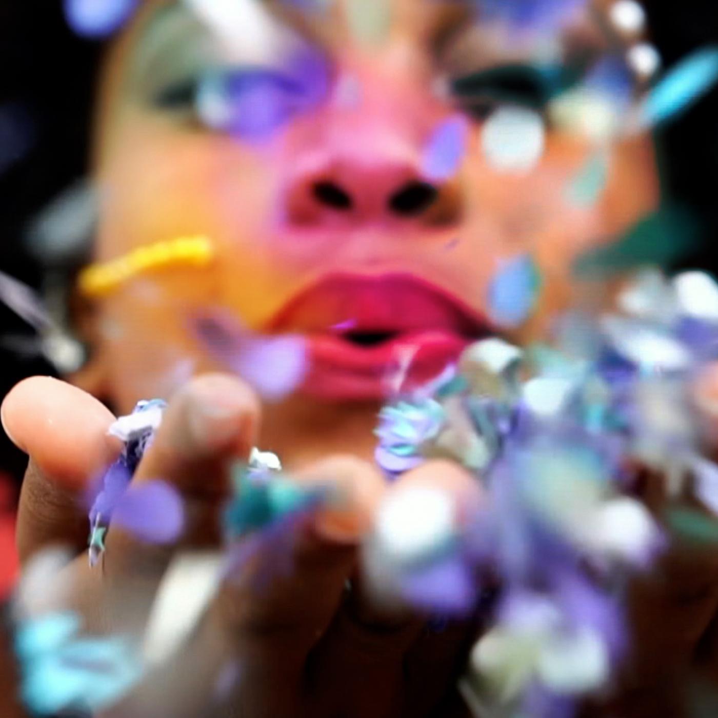 Ein rot bemalter Mund bläst in Blütenblätter