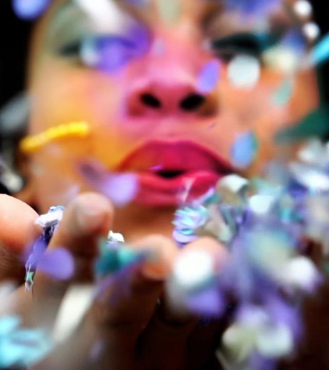 Ein rot bemalter Mund bläst in Blütenblätter