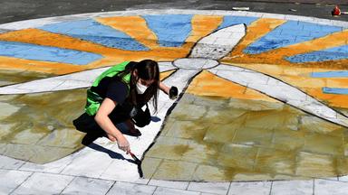 Eine Fridays for Future-Aktivistin malt ein Windkraftrad vor Sonne auf den Boden