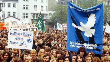 Eine große Menschenmenge demonstriert mit großen Plakaten, auf denen unter anderem eine Friedenstaube zu sehen ist.