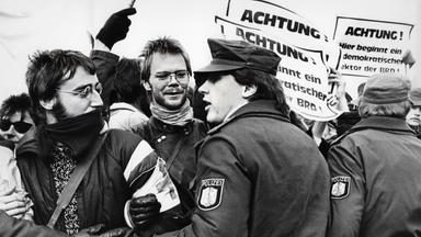 Polizisten drängen bei einer Demonstration Männer mit Plakaten zurück.