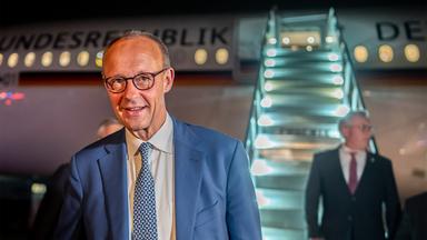 Ein Mann im Anzug steht glücklich lächelnd vor einem Flugzeug, an das eine Rolltreppe angedockt ist.