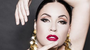 Portraitfoto von Sonya Yoncheva. Sie trägt ein schwarzes, schulterfreies Abendkleid. Die rechte Hand tippt an den Mund. Den linken Arm hat sie angehoben über den Kopf.