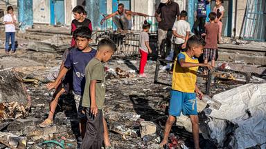 Ein paar Jungs und Männer laufen zwischen den Trümmern im Innenhof eines zerstörten Gebäudekomplexes.