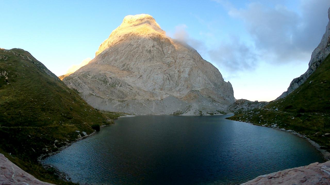 Von Wolken beschattete Bergspitze spiegelt sich unklar in Bergsee