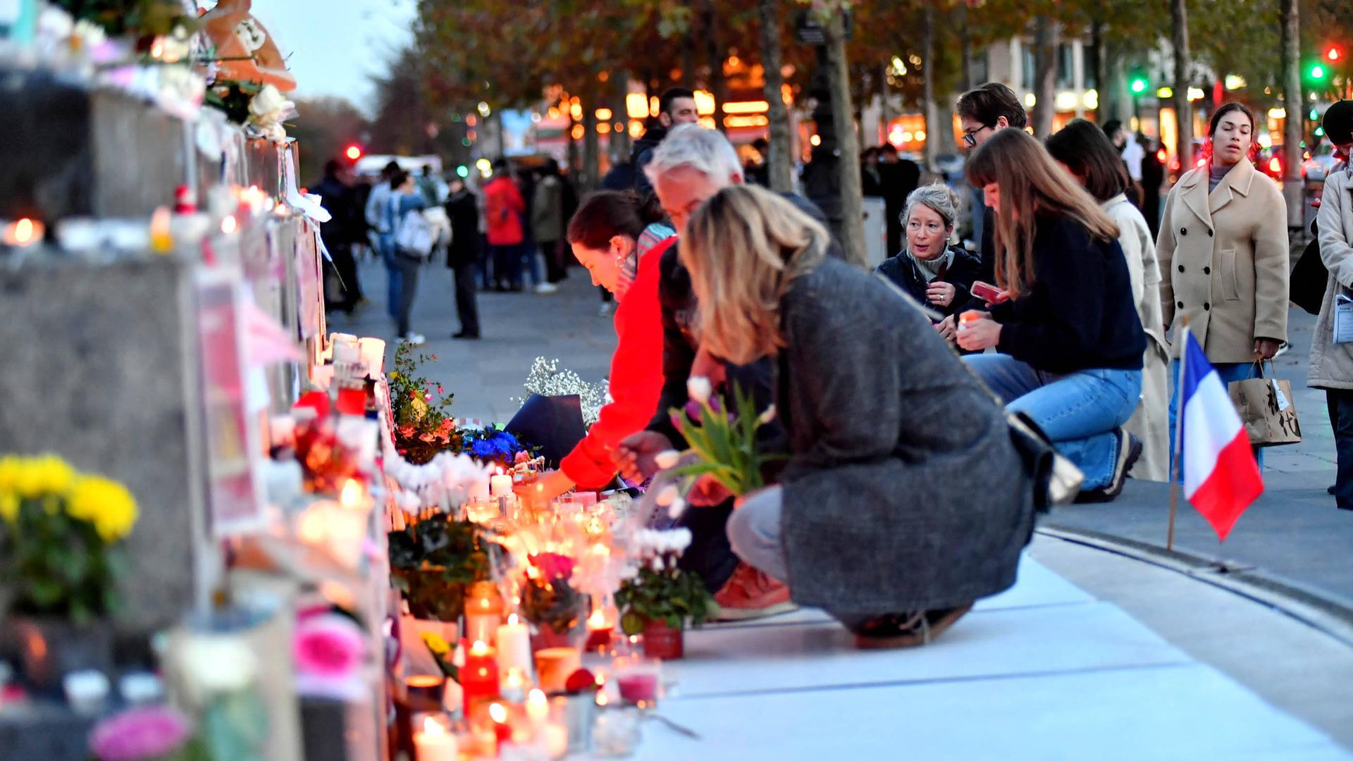 Menschen knien vor abgelegten Kerzen und Blumen.