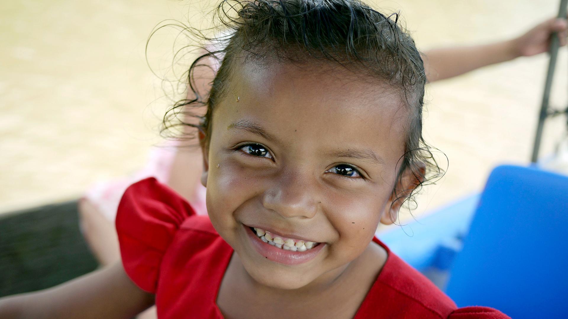 Ein Kind in rotem Kleid strahlt fröhlich in die Kamera.