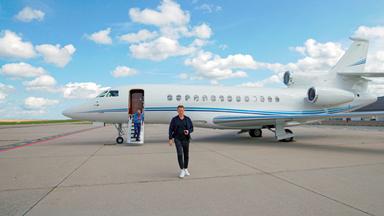 Jochen Breyer geht auf einer Landebahn vor einem privaten Jet.