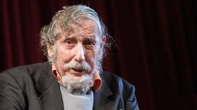 Porträtfoto eines alten Mannes mit schütterem lockigem Haar und Bart.