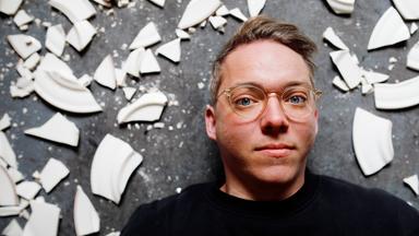 Janik liegt auf dem Boden und schaut in die Kamera. Um ihn herum sind Scherben zu sehen.