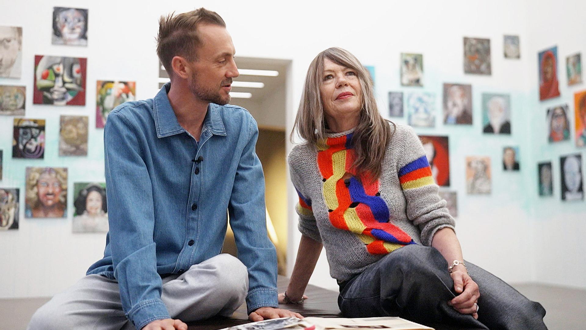 Ein Mann und eine Frau sitzen vor einer Wand mit vielen Bildern