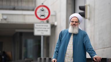Imam Husamuddin Meyer vor einem Straßenschild.