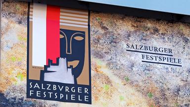 Salzburger Festspiele Logo, Plakat darauf eine stilisierte Maske, eine stilisierte Burg und die Flagge von Salzburg