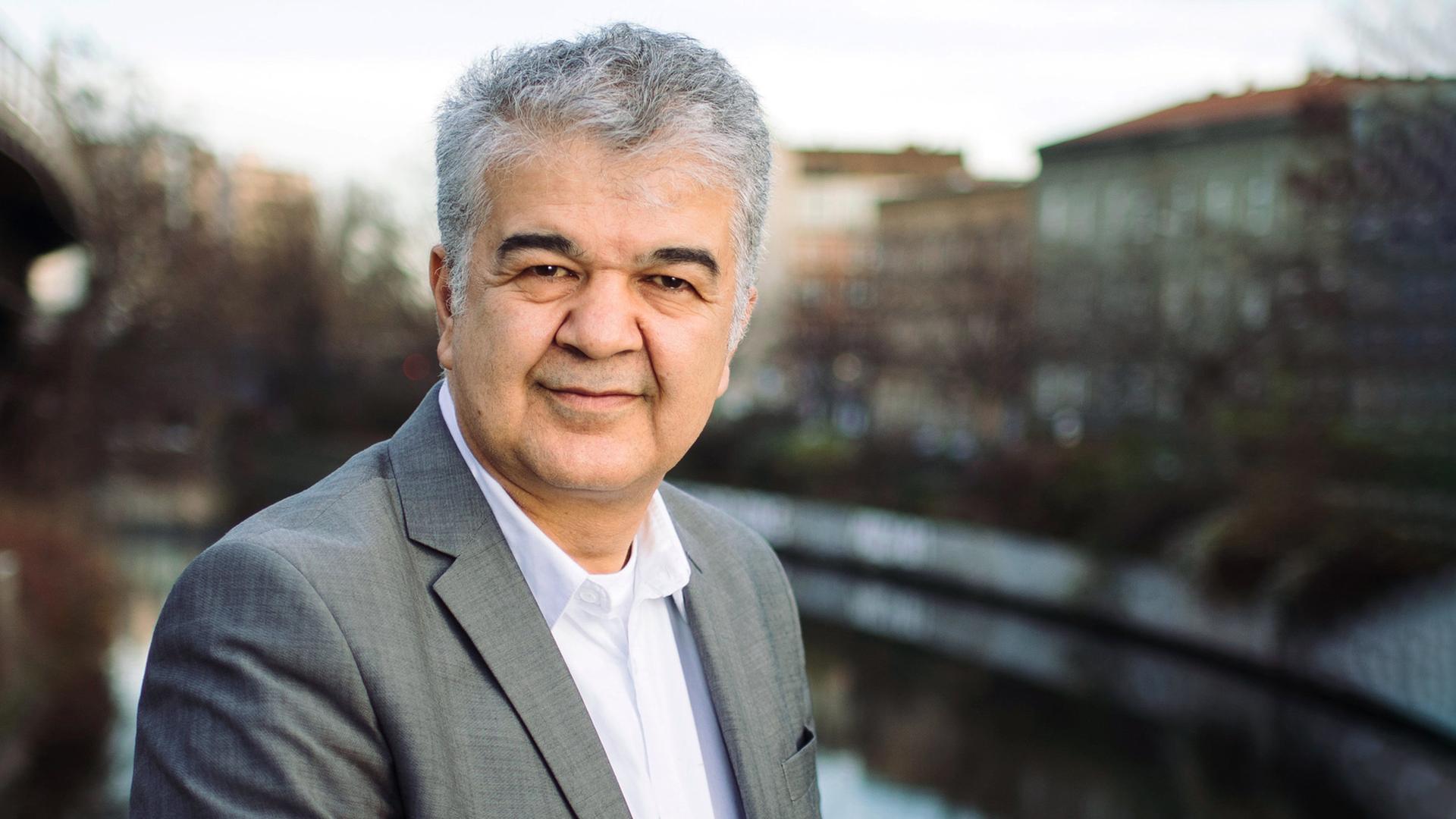 Ein Mann mit grauem Haar und Anzug vor einem verschwommenen Hintergrund.