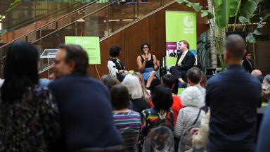 Bei einer Veranstaltung sitzen mehrere Personen auf einem Podium vor Zuschauern und reden.