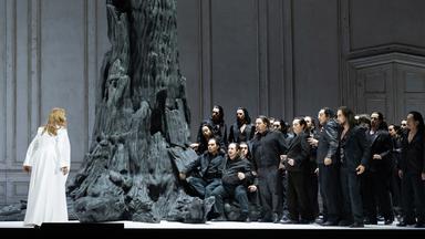 Eine dunkel gekleidetet Menschenmenge steht einer Frau im weissen Kleid gegenüber